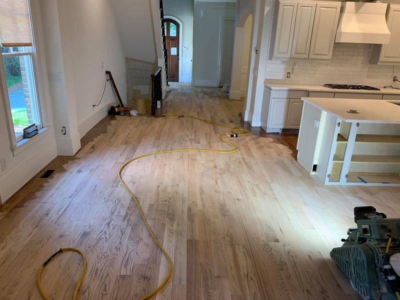 Kitchen floor partway through sanding with a sander and cords on the floor